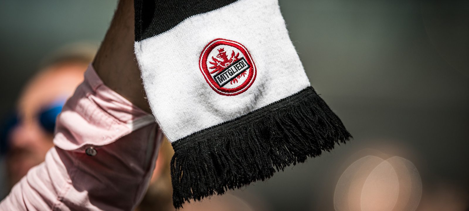 Ein Fan hält einen schwarz-weißen Schal mit dem Logo von Eintracht Frankfurt hoch. Im Hintergrund sind unscharf weitere Fans zu sehen.