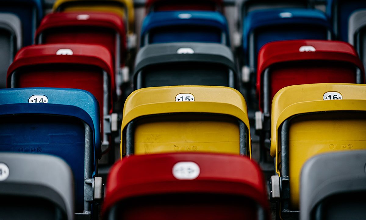 Eine Nahaufnahme von Stadion-Sitzreihen in verschiedenen Farben, darunter blau, rot, gelb und grau. Jeder Sitz ist mit einer Nummer versehen, wobei die Nummern 14, 15 und 16 deutlich sichtbar sind.