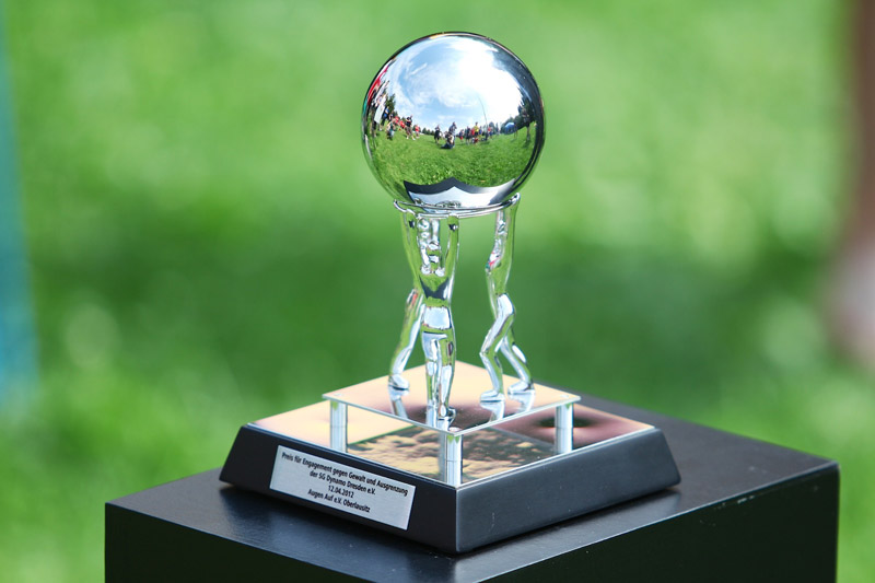 Ein gläserner Pokal mit einer spiegelnden Kugel oben drauf, der auf einem schwarzen Sockel steht. Im Spiegel der Kugel ist ein Fußballfeld mit Spielern zu sehen. Der Pokal ist der SGD-Preis für den nachhaltigsten Verein der Bundesliga.