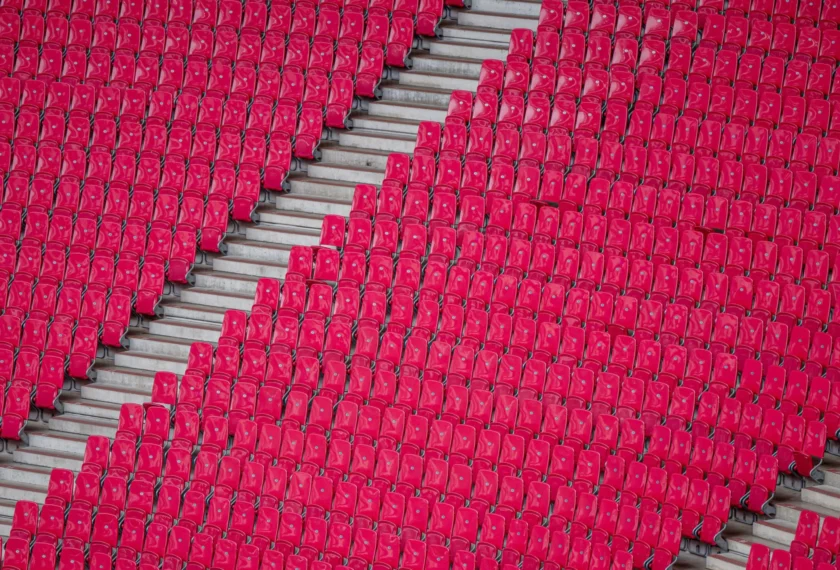 Rote Sitzplätze in einem Fußballstadion, die in einem Muster angeordnet sind, das an ein Herz erinnert. Die Sitze sind leer und das Bild zeigt eine Nahaufnahme der Sitzreihen.