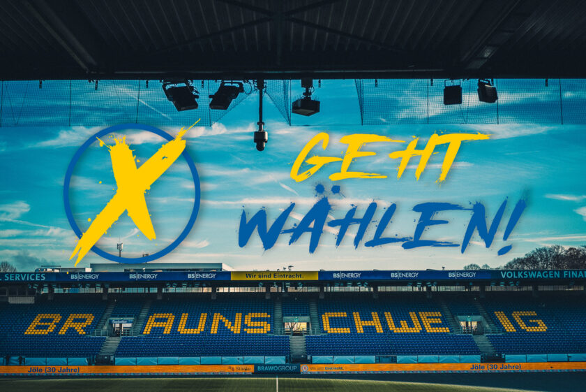 Ein Stadion mit einer großen Werbetafel, auf der "GEHT WÄHLEN!" steht. Im Hintergrund sind die Sitzplätze des Stadions zu sehen, auf denen "EINTRACHT" in großen Buchstaben zu lesen ist.