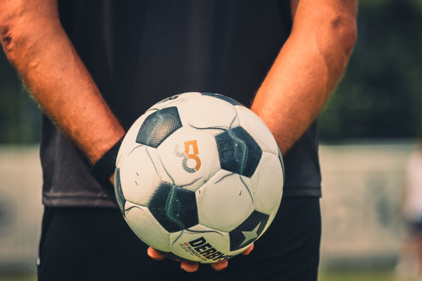 Eine Person hält einen Fußball mit den Händen. Der Ball hat ein schwarzes und weißes Design mit dem Logo der Bundesliga und dem Markennamen "Derbystar".