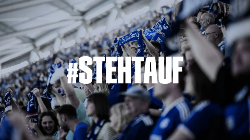 Eine Menschenmenge in einem Stadion, die blau-weiße Schals schwingt und jubelt. Im Vordergrund ist der Hashtag "#STEHTAUF" prominent zu sehen.