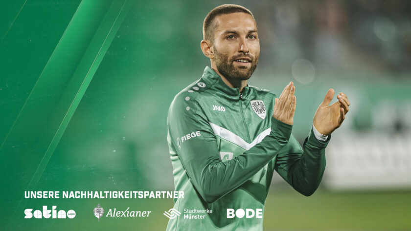 Ein Fußballspieler in grünem Trikot mit weißem V-Ausschnitt und der Nummer 7 auf der Brust steht auf dem Spielfeld und klatscht in die Hände. Im Hintergrund sind grüne Lichtstreifen zu sehen. Am unteren Bildrand befinden sich die Logos der Nachhaltigkeitspartner: satino, Alexianer, Stadtwerke Münster und Bode.