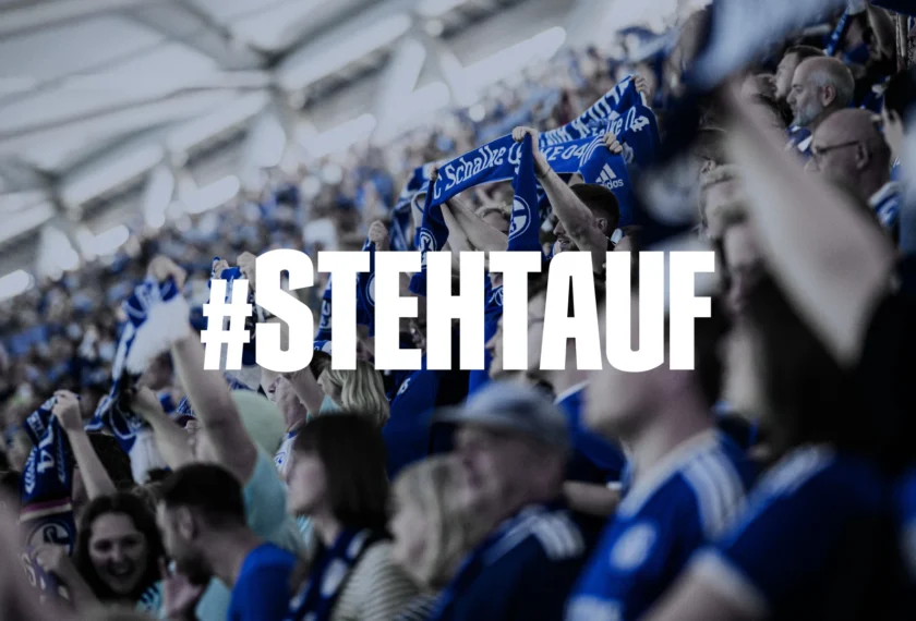 Fans im Stadion, die blau-weiße Schals schwenken und stehen, mit dem Hashtag "#STEHTAUF" im Vordergrund.