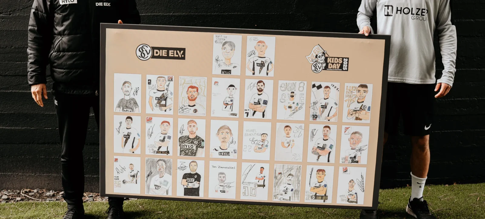 Zwei Personen halten ein Plakat mit Zeichnungen von Fußballspielern in Trikots. Die Zeichnungen sind mit den Namen und Nummern der Spieler versehen und teilweise mit Signaturen. Das Plakat ist Teil des "Kids Day" der DFL und zeigt verschiedene Spieler des SV Diez.