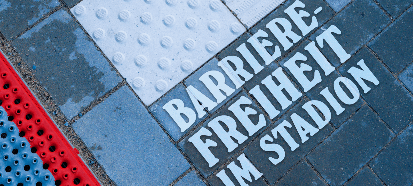 Bodenbelag mit der Aufschrift 'Barrierefreiheit im Stadion' in weißer Schrift auf blauem Untergrund. Der Belag hat taktile Elemente für sehbehinderte Menschen.