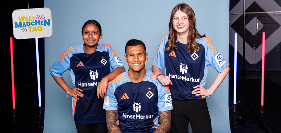 Drei Personen, zwei Frauen und ein Mann, stehen lächelnd nebeneinander und tragen blaue Trikots mit dem Aufdruck "HanseMerkur" und dem Logo des HSV. Im Hintergrund ist ein Schild mit der Aufschrift "Welt MädchEN Tag" zu sehen. Die Personen posieren vor einem blauen Hintergrund mit geometrischen Mustern und pinken Lichtstreben.