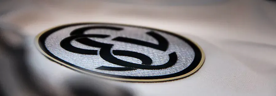 Ein ovales Logo mit einem stilisierten Fußball in der Mitte, umgeben von zwei geschwungenen Linien, die sich überkreuzen. Das Logo ist in Schwarz und Weiß gehalten und befindet sich auf einem weißen Hintergrund.