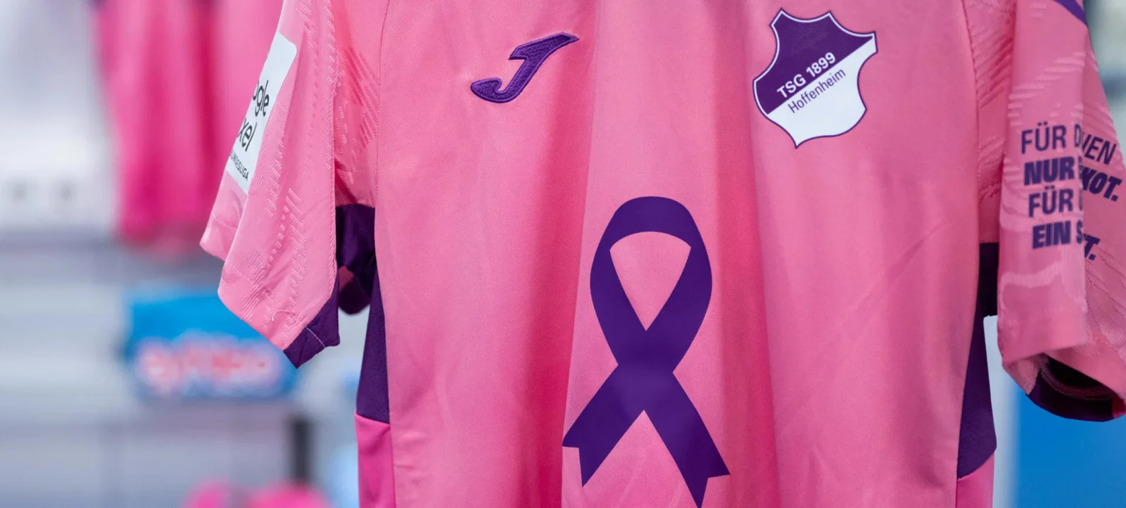 Ein pinkfarbenes Trikot des TSG Hoffenheim mit einem lila Brustkrebs-Awareness-Schleife und dem Vereinswappen.