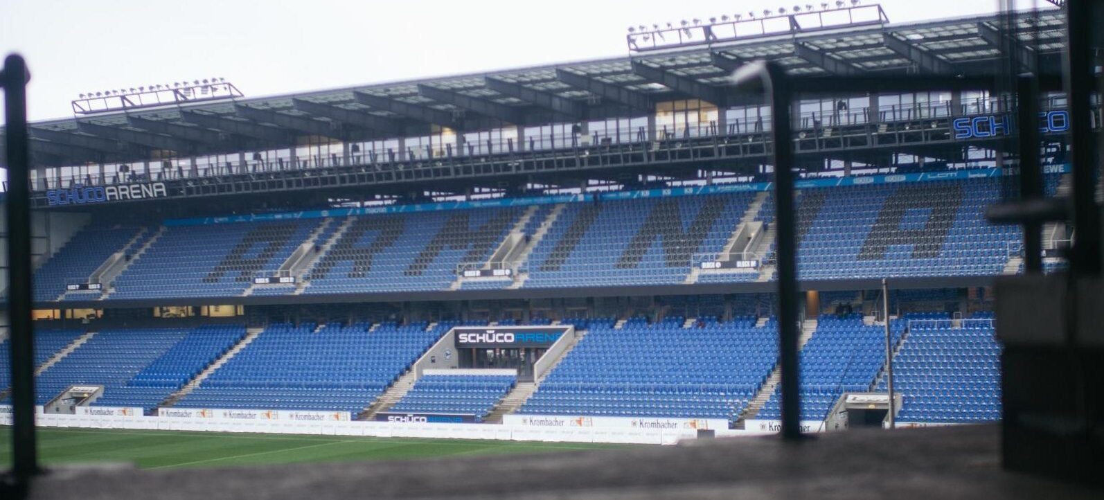 Ein Blick auf das leere Stadion der Schüco Arena, mit blauen Sitzplätzen und einem Blick auf den Rasen.