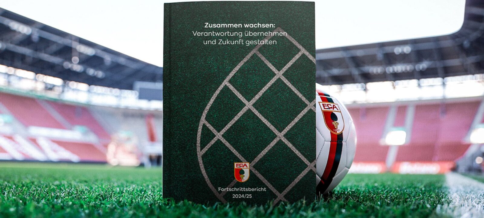 Ein Bericht mit dem Titel "Zusammen wachsen: Verantwortung übernehmen und Zukunft gestalten" liegt auf einem Fußballfeld. Im Hintergrund ist ein Teil der Stadiontribüne zu sehen.