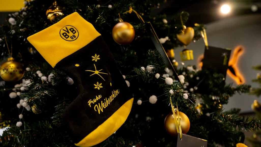 Ein Weihnachtsbaum mit goldenen Kugeln und einem schwarzen und gelben Socken mit dem BVB-Logo und der Aufschrift "Frohe Weihnachten".